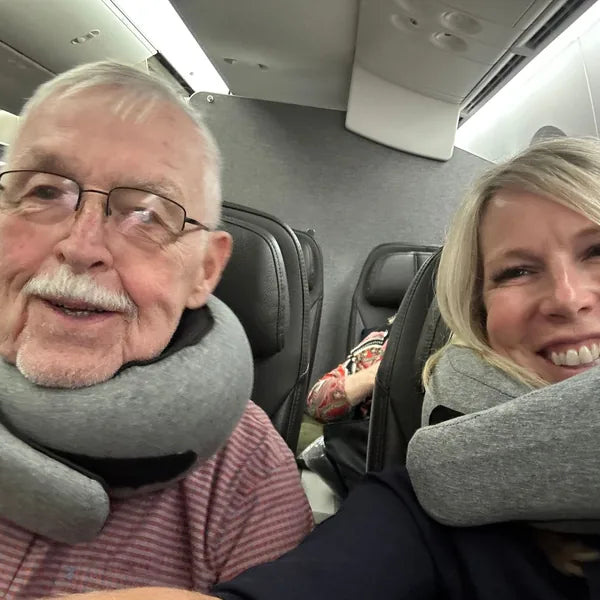 An older couple on a plane, one wearing the WANDER+ Pillow