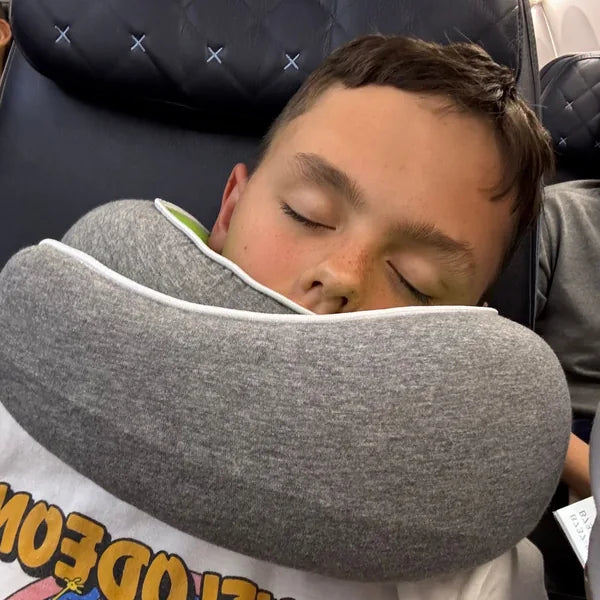 A child asleep in the back seat of a car wearing the WANDER+ Pillow